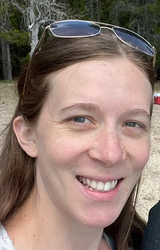 A woman smiling for the camera with her hair in front of her face.